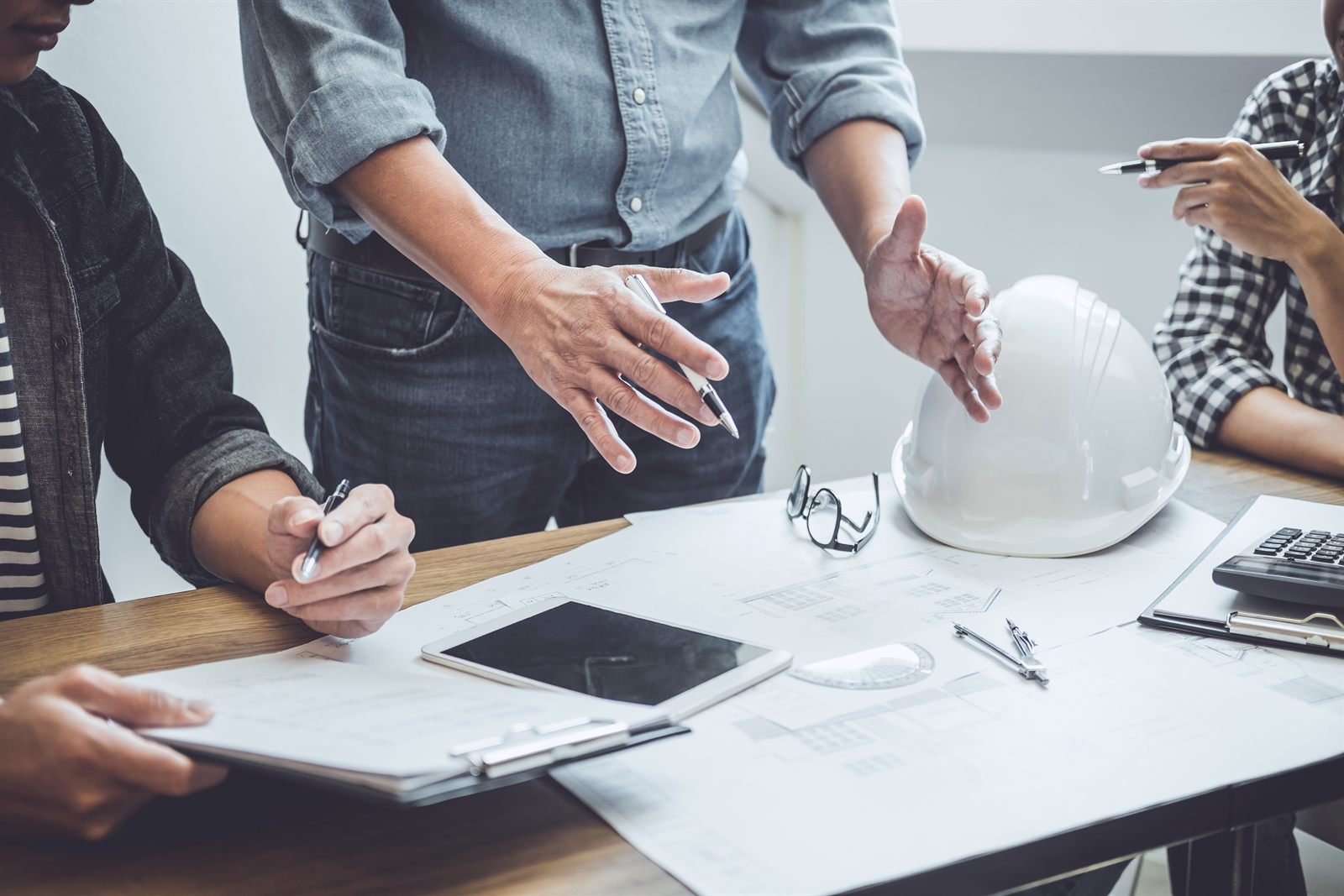 Projektový tým nad výkresy a tabletem, vedle leží stavební přilba